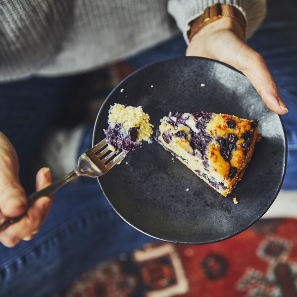 Une personne assise sur un tapis qui mange une part de gâteau aux bleuets. 