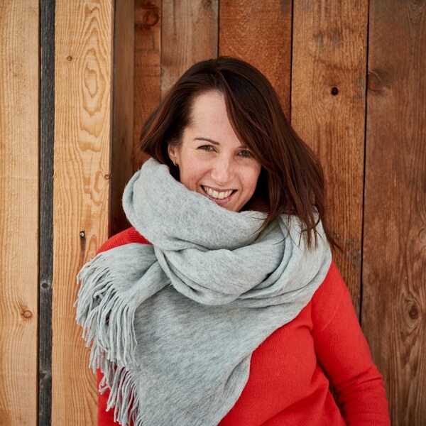 Geneviève O'Gleman portant un gros foulard, devant un mur en bois. 