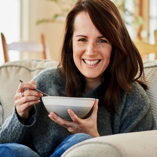 Geneviève O'Gleman assise sur un canapé et qui tient un bol de soupe.