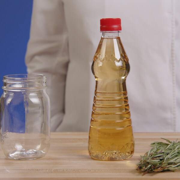 Un pot en vitre, une bouteille de vinaigre et un bouquet de fines herbes sont posés sur une place de travail. 
