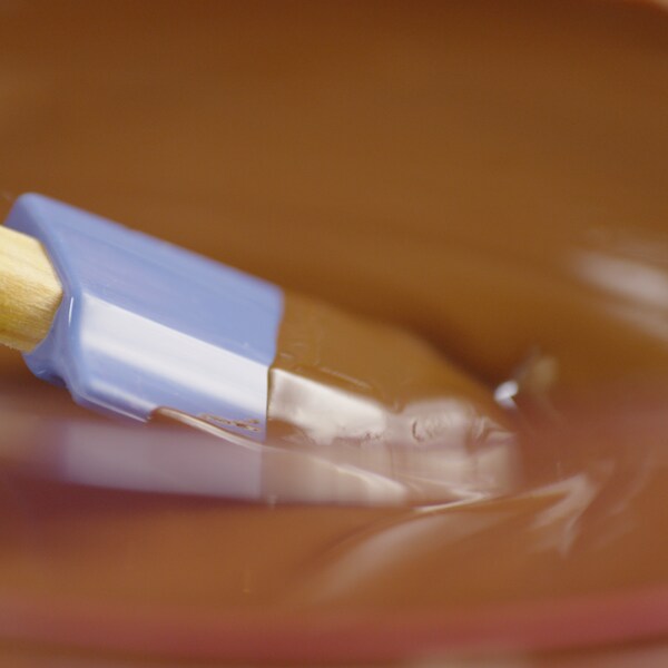 Une personne touille doucement une sauce au chocolat avec une spatule souple. 