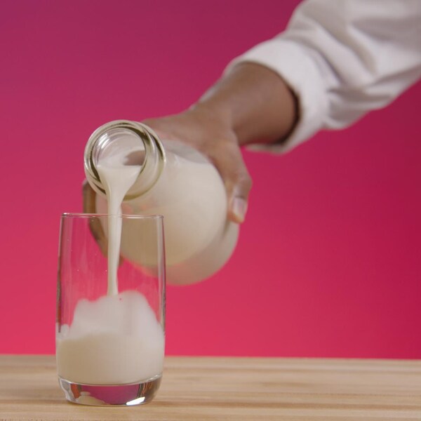 Une personne verse du lait d'amande dans un grand verre en vitre.