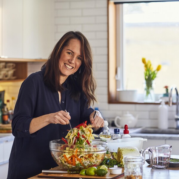 Il est possible de voir Geneviève dans la cuisine en train de préparer une salade. Elle sourit à la caméra.