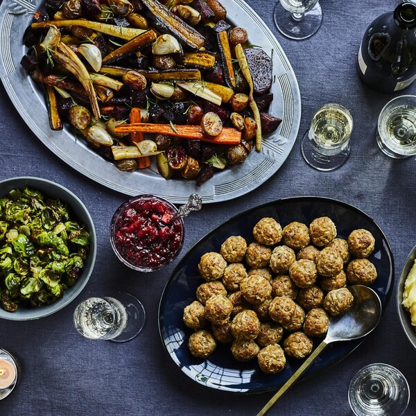 Table festive avec un plat de légumes rôtis, une salade verte, un plat de boulettes de viande et un bol de purée de pommes de terre.