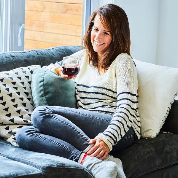 La nutritionniste Geneviève O'Gleman est assise sur un sofa, un verre de vin rouge à la main.