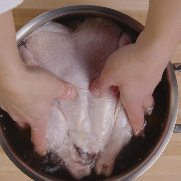 Une personne plonge un poulet cru dans une casserole contenant de la saumure. 