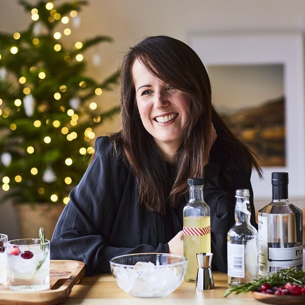 La nutritionniste Geneviève O'Gleman est assise, souriante, devant des drinks et des bouteilles de spiritueux. Elle est dans un décor de Noël.