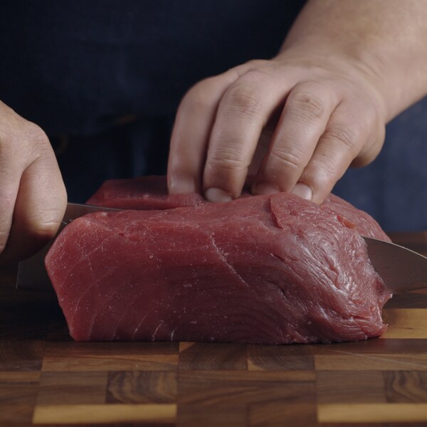 Une personne coupe une partie du thon au moyen d'un couteau bien affuté sur une planche de travaille. 