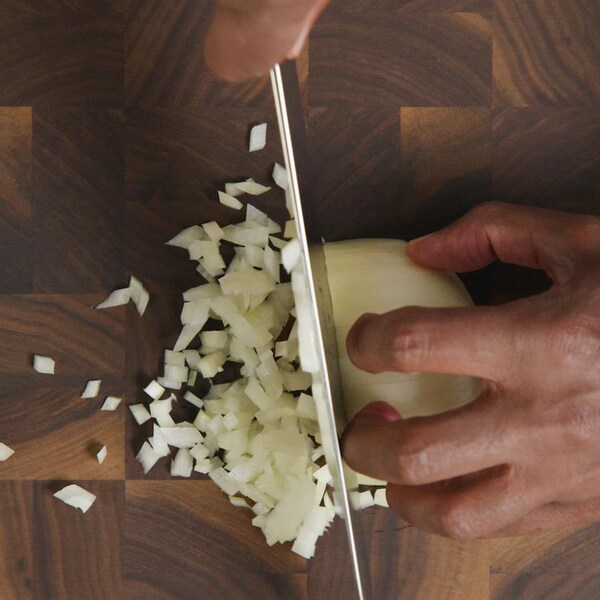 Un oignon tenu par une main alors qu'il se fait trancher par un couteau. 
