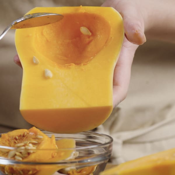 Une personne retire les graines d'une courge musquée en utilisant une cuillère. 