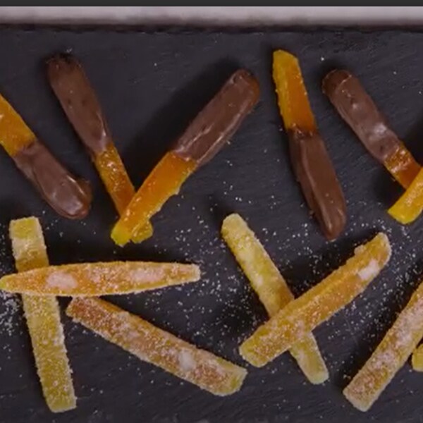 Des zestes d'agrumes confits nature et trempés dans le chocolat sur une plaque de cuisson. 