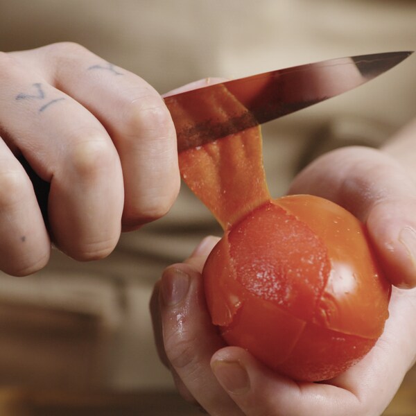 Une personne a une main un petit couteau et une tomate italienne. 