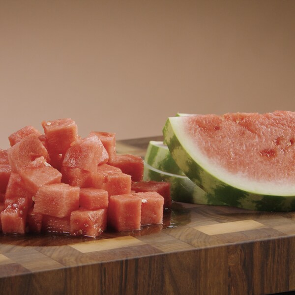 Un melon d'eau a été coupé en tranche et en cube. Les morceaux sont posés sur une table de travail. 