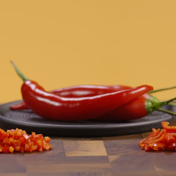 Des poivrons épicés sont dans une assiette ronde et devant ceux-ci des morceaux ont été hachés et coupés en tranches. 