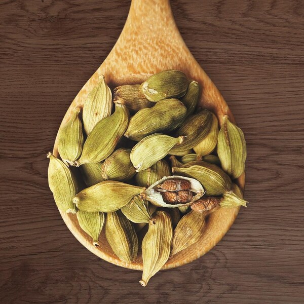 Plusieurs graines de cardamomes dans une cuillère en bois.