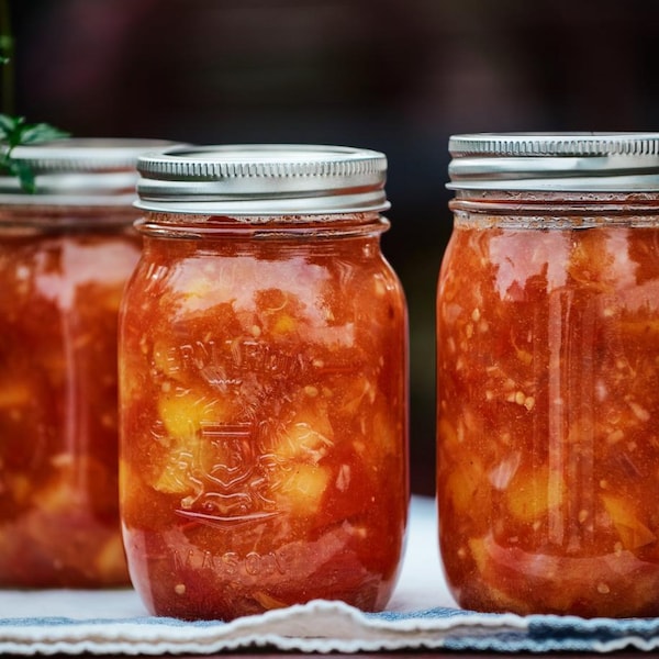 Des conserves de chutney aux tomates et aux pêches déposées sur un linge.