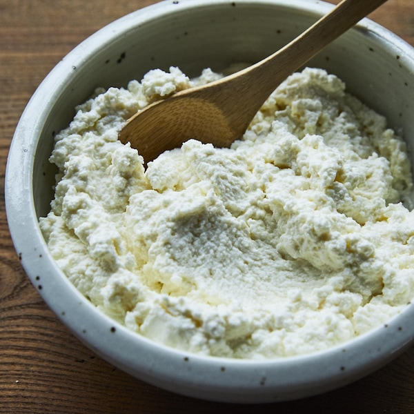 Un bol rempli de ricotta avec une petite cuillère en bois dedans. 