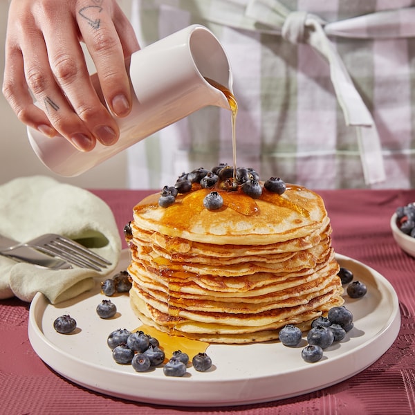 Une assiette avec une grosse pile de pancakes recouverts de bleuets et de sirop d'érable.