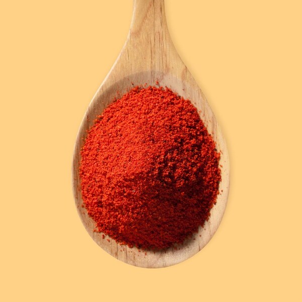 Une cuillère de bois remplie de paprika rouge.
