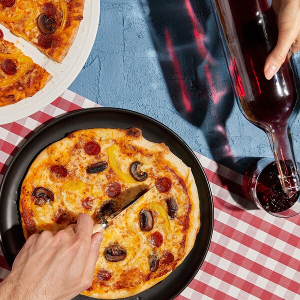 Deux pizzas garnies de pepperonis et de champignons avec des verres de vin rouge.