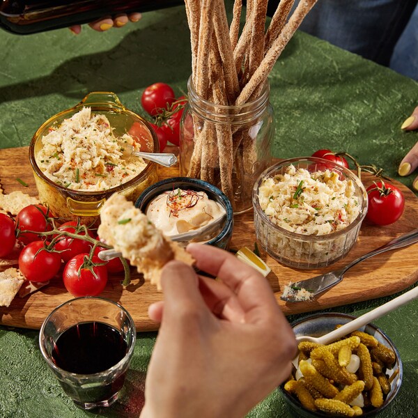 Une planche en bois recouverte de petites tomates en grappe, de petits craquelins, d'un bol de sauce et de deux bols de rillette.
