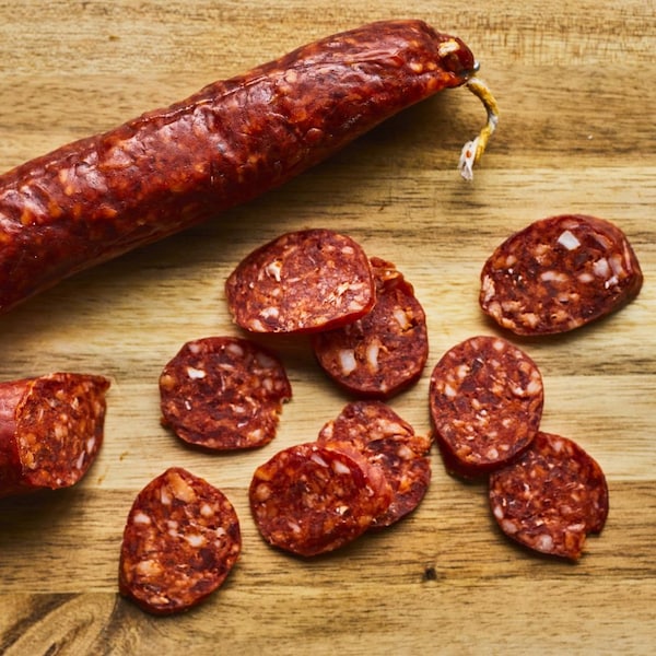 Saucisson chorizo coupé en partie avec des rondelles de chorizo sur une planche de bois.