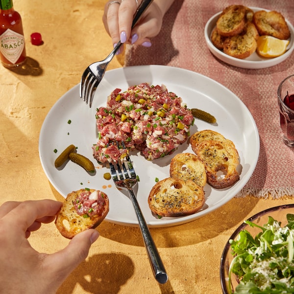 Du tartare de bœuf servi avec des croûtons et de petits cornichons.