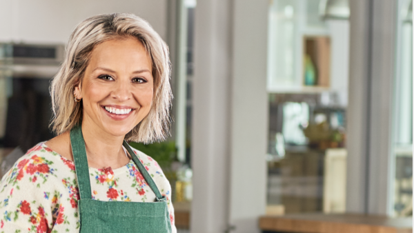 Isabelle Deschamps-Plante dans sa cuisine, habillée d'un chandail fleuri et d'un tablier vert.