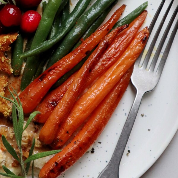 Dans une assiette, il y a des carottes grillées à l'érable avec des petites fèves vertes.