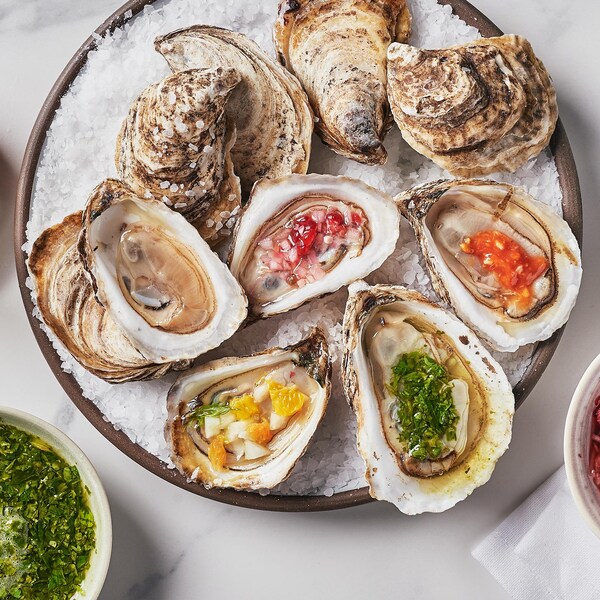 Une assiette contenant des huîtres ouvertes. Tout autour se trouvent des petits bols contenant différent types de mignonnettes.