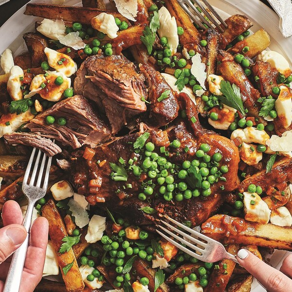 Un plat contenant des frites, un morceau de porc braisé, du fromage en grains et des petits pois frais. Le tout accompagné d'une sauce au vin rouge.