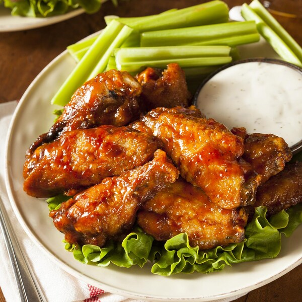Des ailes de poulet dans une assiette avec des morceaux de céleri et un bol de sauce au bleu.