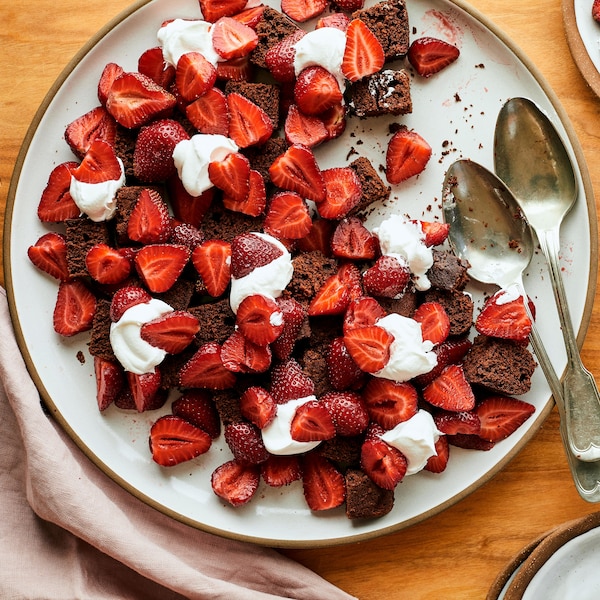 Sur une table en bois, est déposé une grande et deux petites assiettes contenant de la bagatelle choco-café aux fraises. 