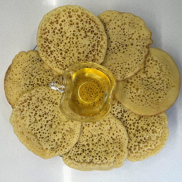 Des petites crêpes disposées dans une assiette avec un petit pot de miel au centre.