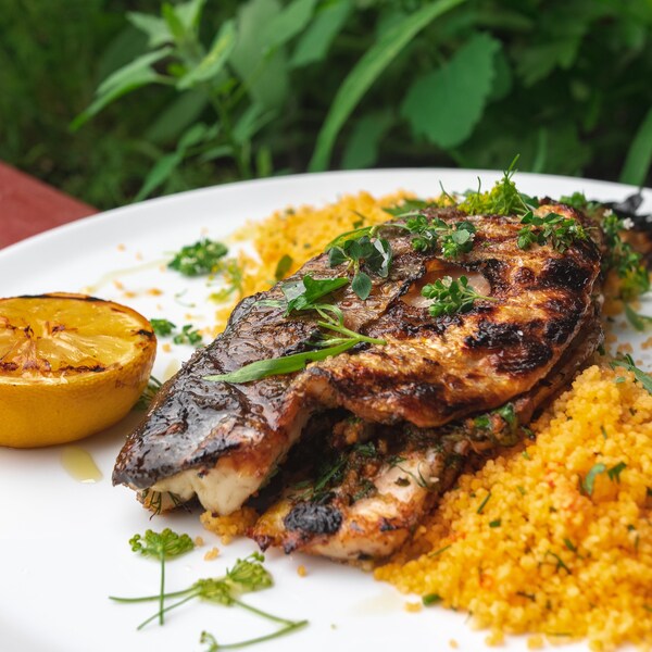Un plat de bar farci au barbecue accompagné de couscous et d'un demi-citron grillé.
