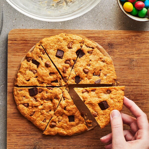 Une main prend un morceau d’un grand biscuit coupé en pointes sur une planche en bois. Autour, il y a plusieurs bols de garnitures différentes et dans le coin supérieur gauche, un second biscuit sort de la friteuse à air.