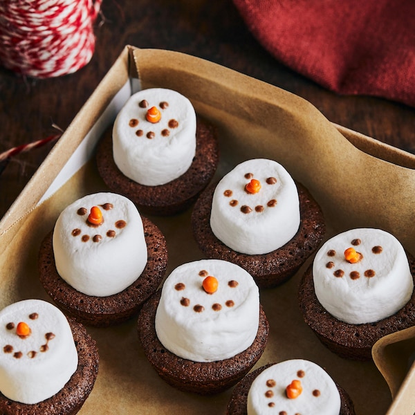 Des bonhommes de neige en brownies sont dans une boîte-cadeau. À côté, il y a une bobine de fil rouge et des petits ciseaux.