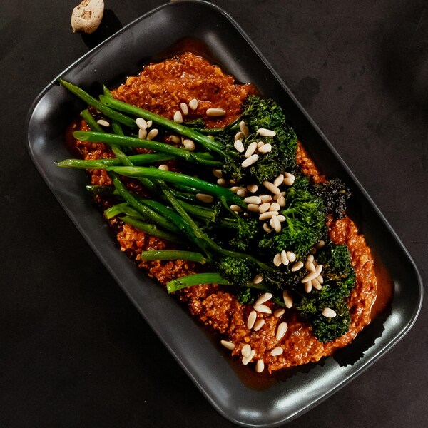 Des broccolinis déposés sur de la sauce romesco dans une assiette.