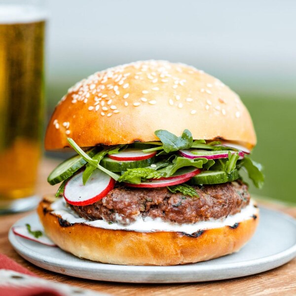 Un burger au bœuf avec des concombres, des radis, de la roquette et une sauce au yogourt.