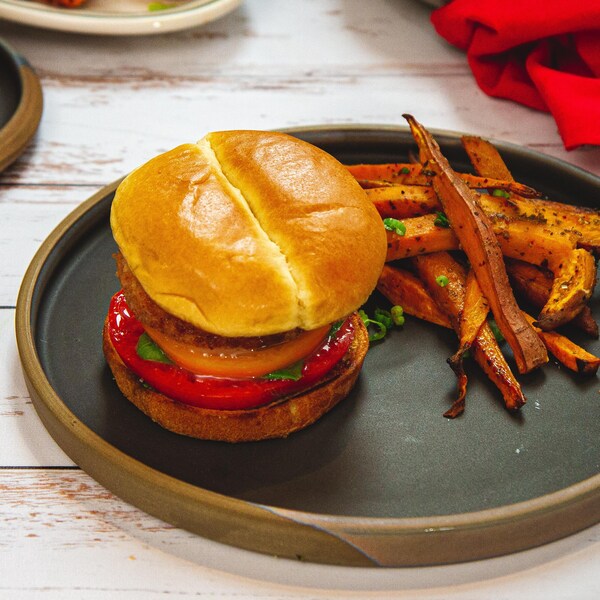 Un burger de fromage servi avec des tranches de tomates, du pesto de basilic et des frites de patates douces.