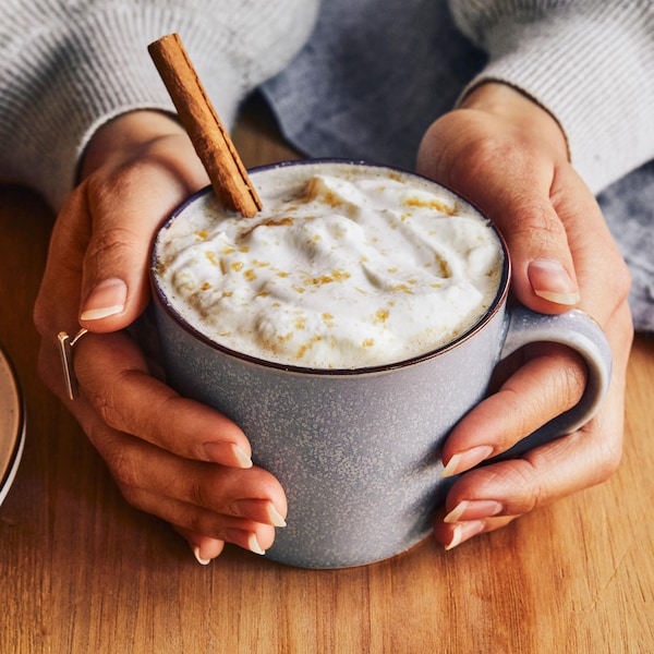 Des mains qui tiennent une tasse remplie de café latté à la brioche à la cannelle.