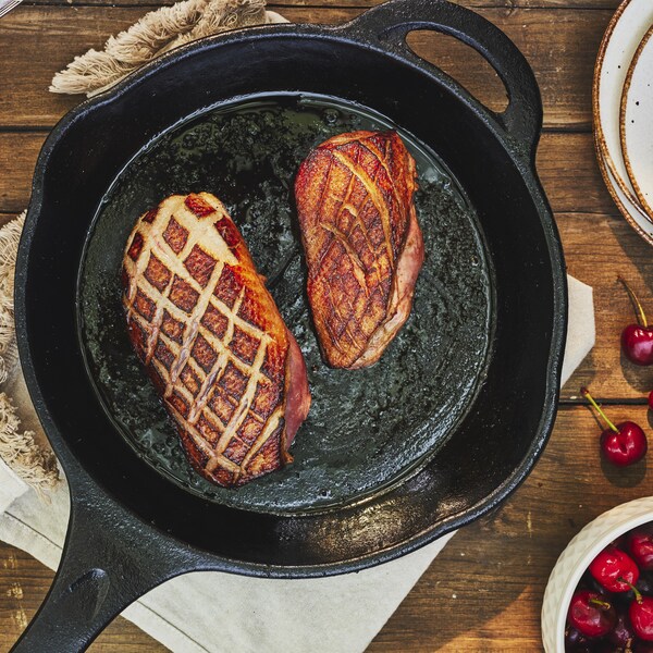 Deux poitrines de canard dans une poêle avec une sauce aux cerises dans un bol.