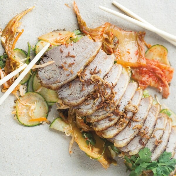 Des tranches de canard laqué dans une assiette de service accompagnées de kimchi.
