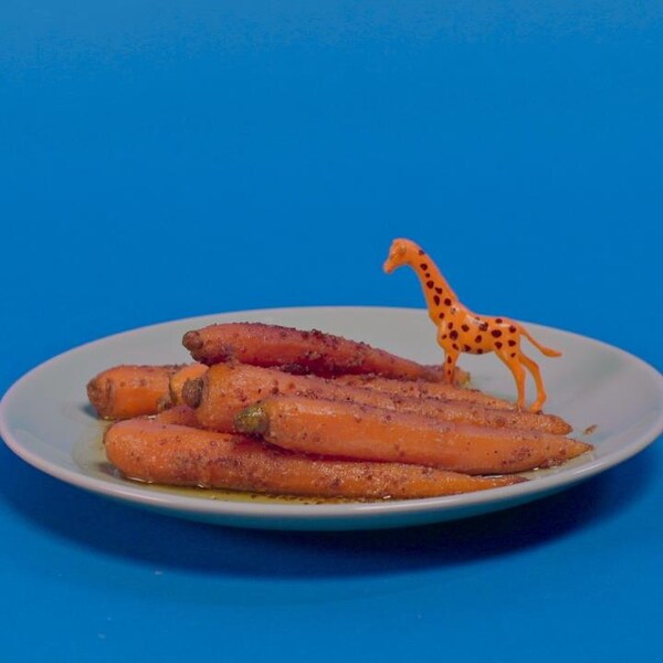 Une assiette de carottes glacées, sur lesquelles se repose une petite girafe de plastique orange.