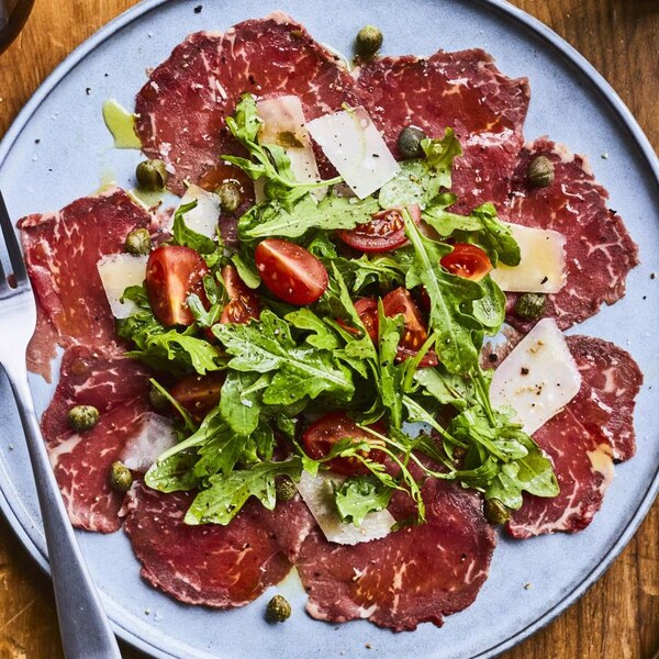 Une assiette de carpaccio de bœuf garni de câpres, de feuilles de roquette, de copeaux de parmesan et de
tomates cerises.