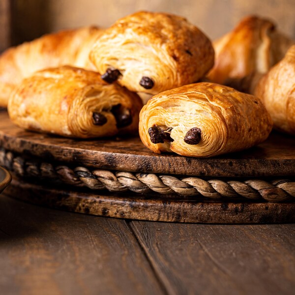 Des pains au chocolat (chocolatines) sur un plateau et une tasse de café.