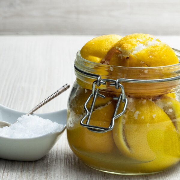 Des citrons confits dans un pot avec un petit bol rempli de gros sel à côté.