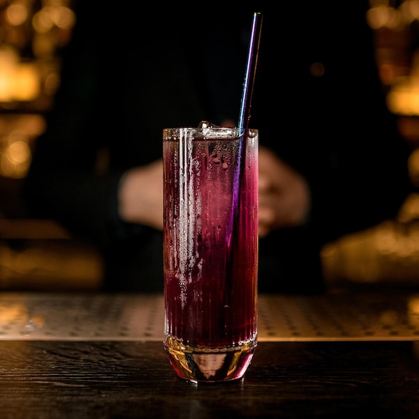 Un cocktail de couleur mauve foncé avec une paille sur comptoir de bar.