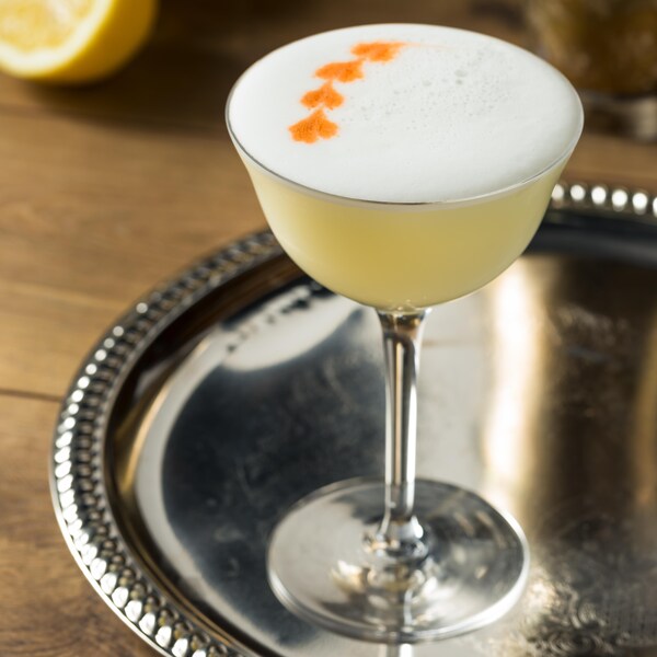 Un cocktail jaune et mousseux dans un verre sur pied présenté sur un plateau d'argent.