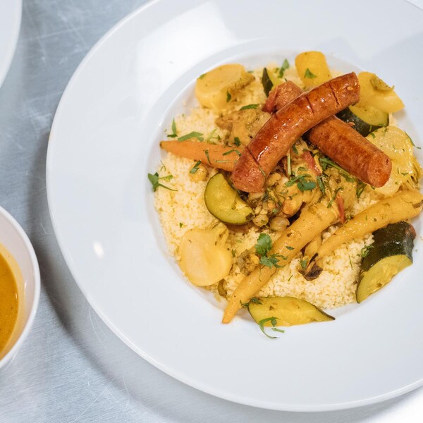 Une assiette de couscous au poulet et merguez, avec des légumes en garniture.